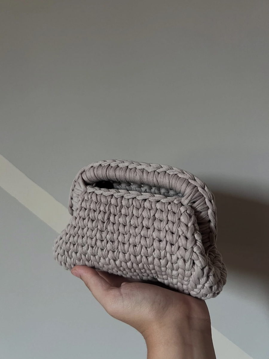 La pouch Nuvola in filato tortora con bordo intrecciato, tenuta in mano